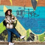 Emily exploring Grand Forks in front of a graffiti wall pointing to the words "Grand Forks"