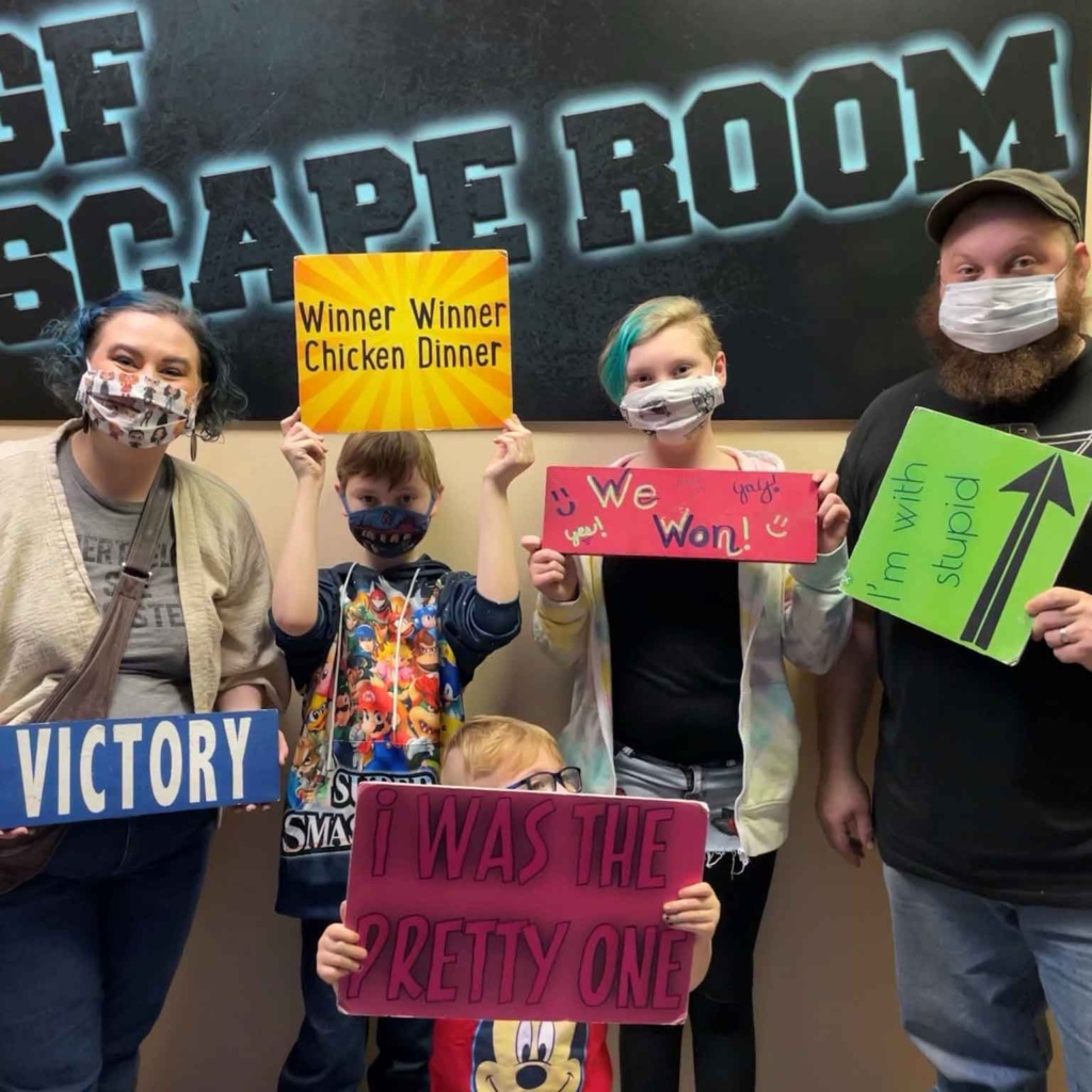 Mom, dad, and 3 Ferguson children holding signs after escaping the Escape room in Grand Forks