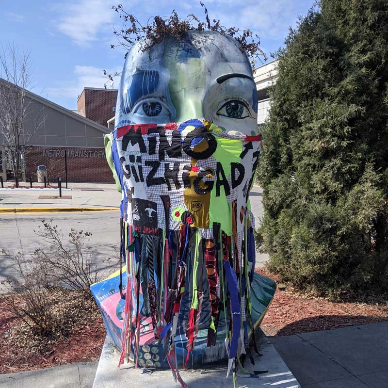 A Blue Head Planter wearing a mask as part of the public art in downtown Grand Forks