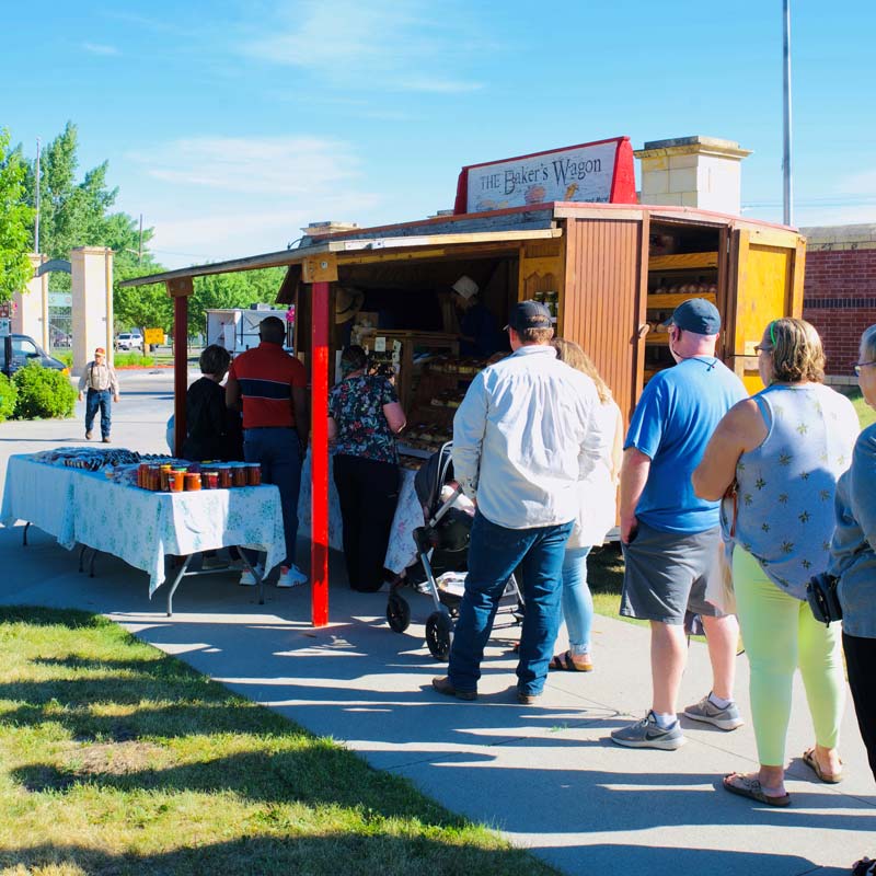 A line of people standing outside the The Baker's Wagon at the downtown farmers market in Grand Forks