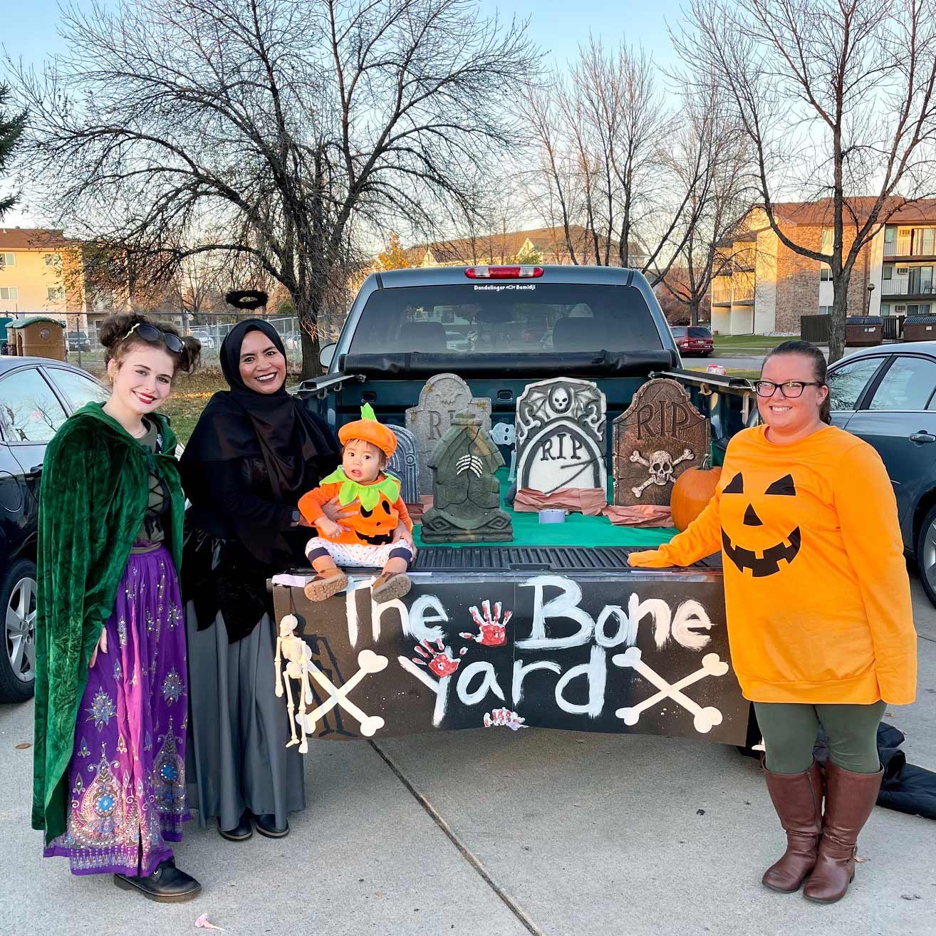 women stand in halloween costumes by decorated truck