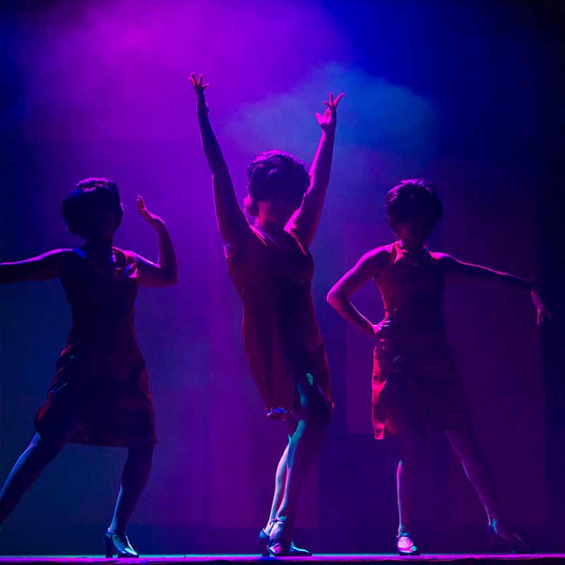 three women performing in purple spotlight on Grand Fork's Stage