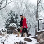 Christmas in the park with snow falling. Couple walks their dog.