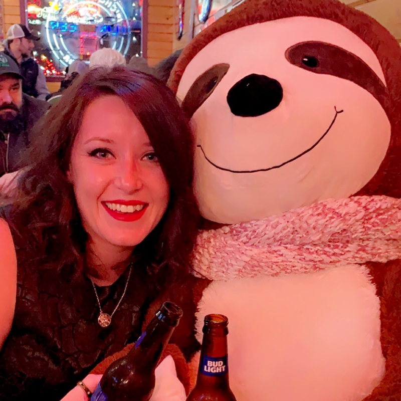 Women poses with plush sloth with beers at Grand Forks Bar