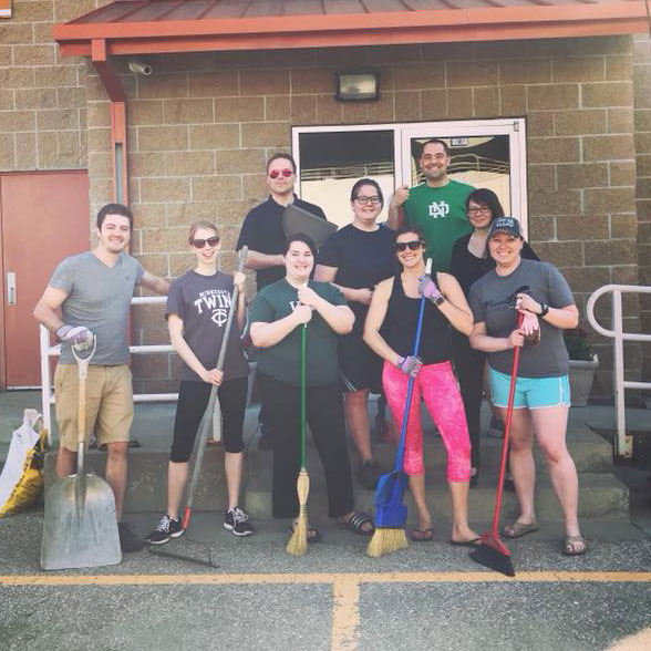 Group of young adults standing with shovels, broom, and tools at Greater Grand Forks Young Professionals volunteer event.