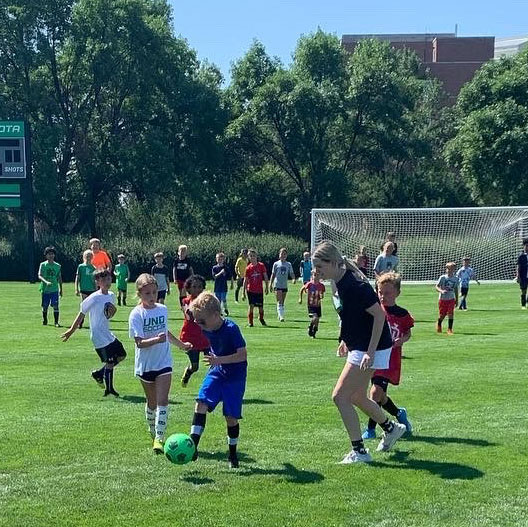 Kids play soccer with coach on field at the University of North Dakota Soccer Camp in Grand Forks, ND