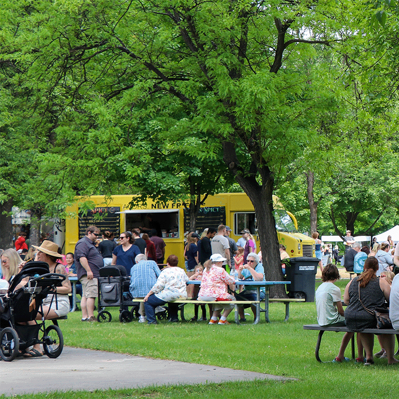Food truck in park with people seated at picnic tables.