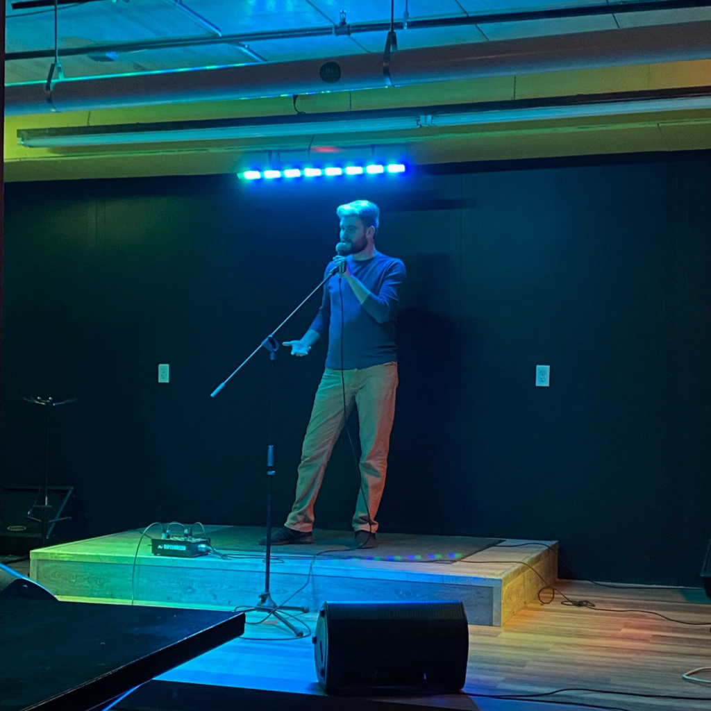 Man standing on a stage at an open mic night in the basement of Half Brothers brewing company