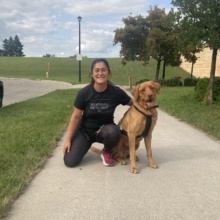 Greenway canicross crop 1 A woman kneels on the ground and poses smiling with a dog.