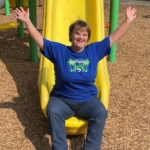 What's Cooler Today author Erin sits on the bottom of a yellow slide with her arms held up.