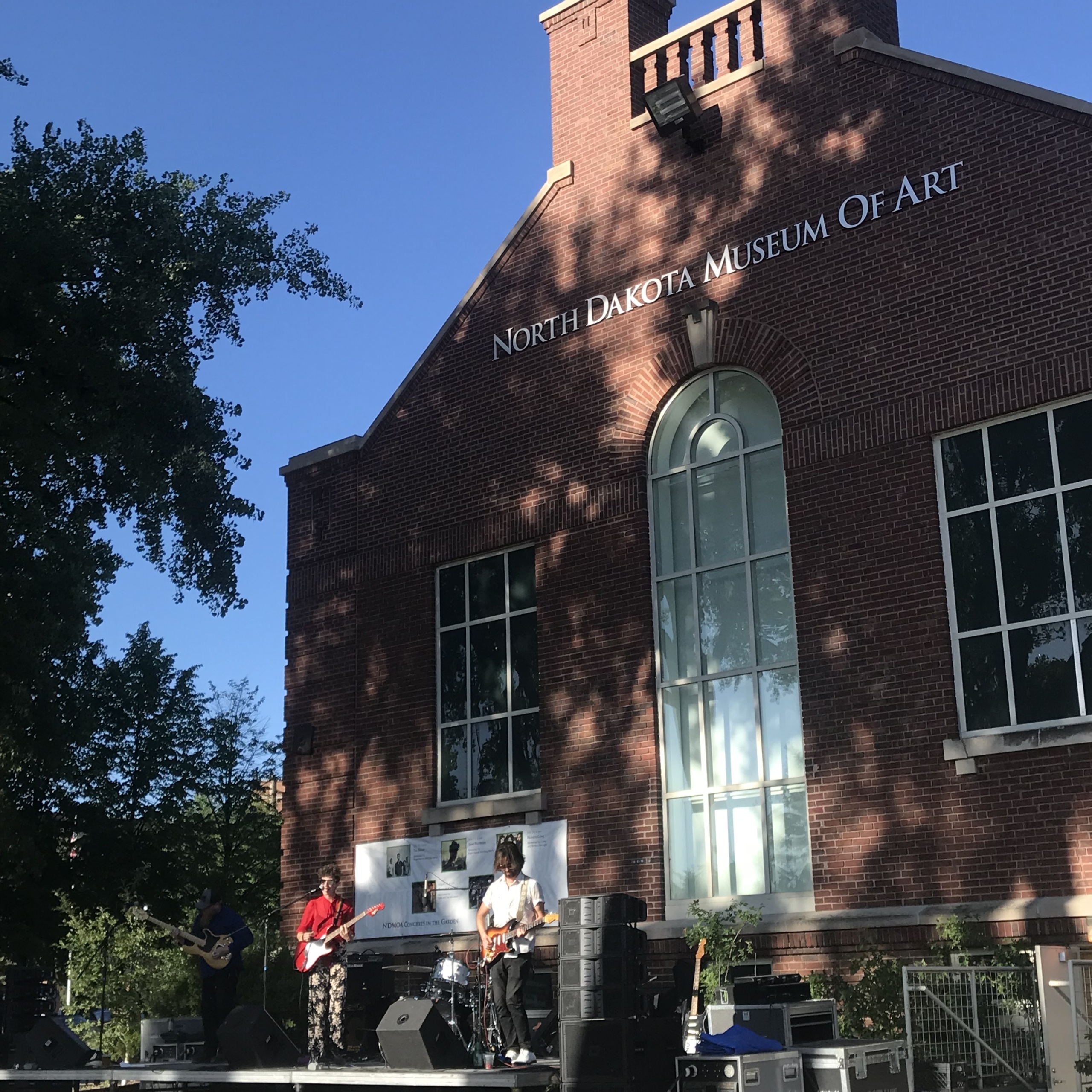 A small band plays on a stage outside of the North Dakota Museum of Art, a large, brick building.
