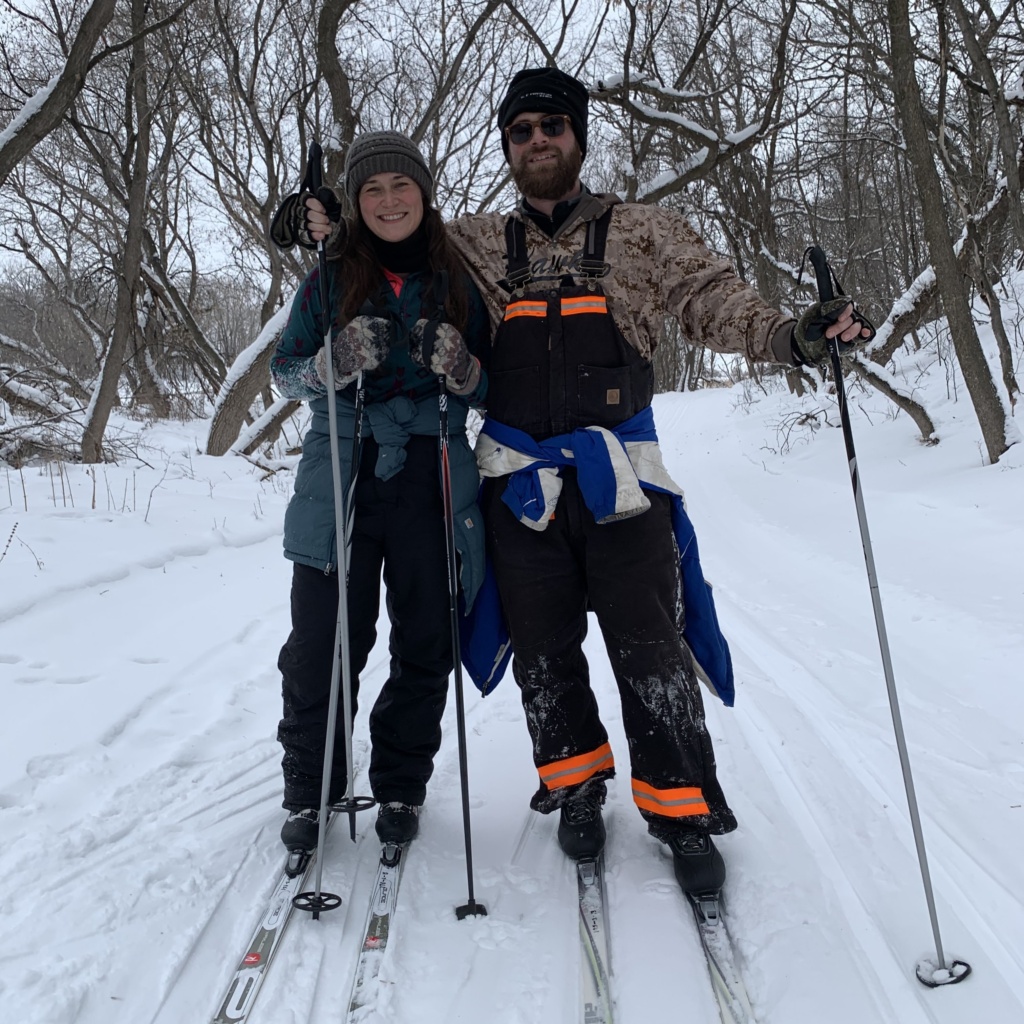 Whats Cooler Today Writer Sally and her partner smile for the camera donning skies, poles and winter gear on well-groomed snowy trails