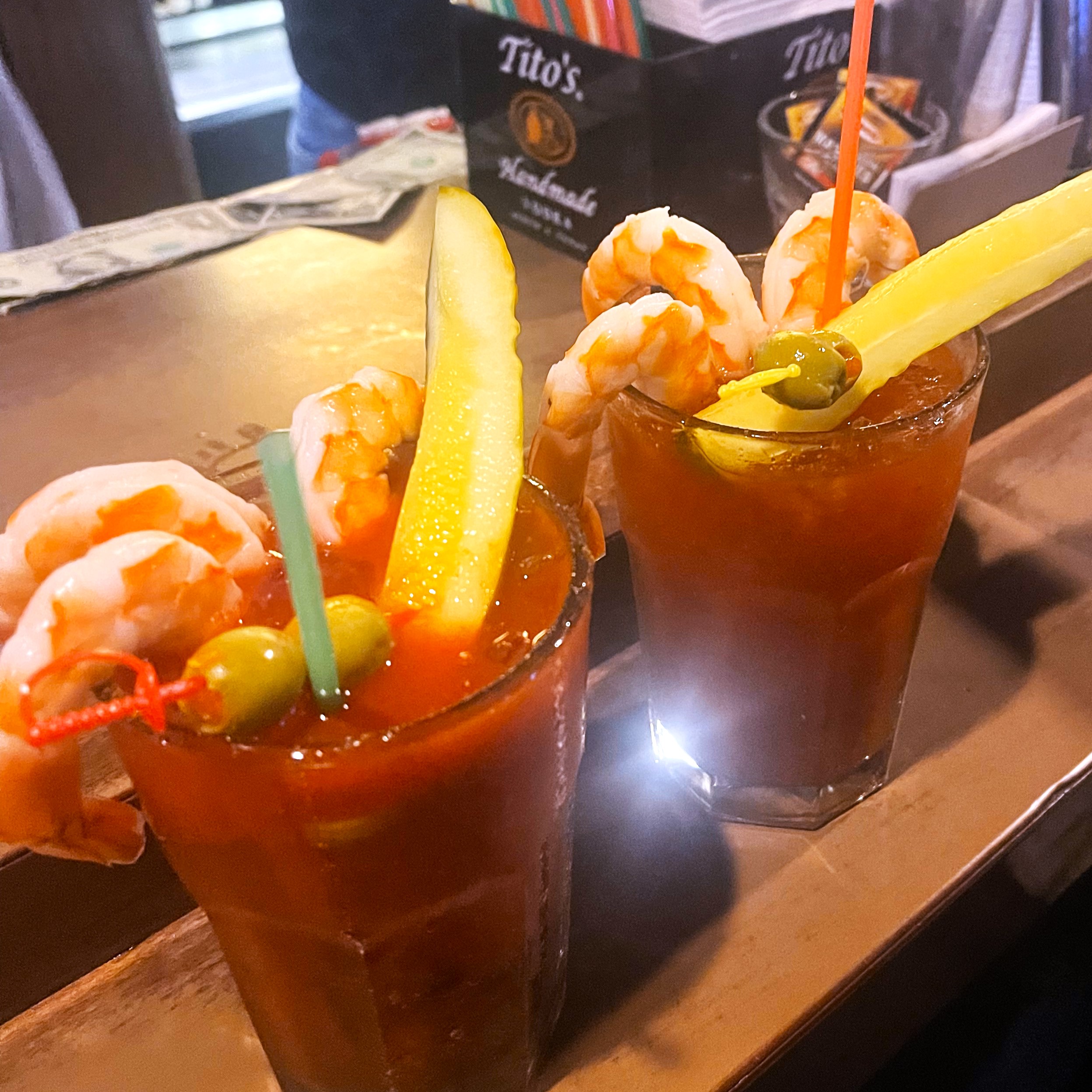 Two glasses filled with bloody marys and toped with pickles, olives, and cocktail shrimp
