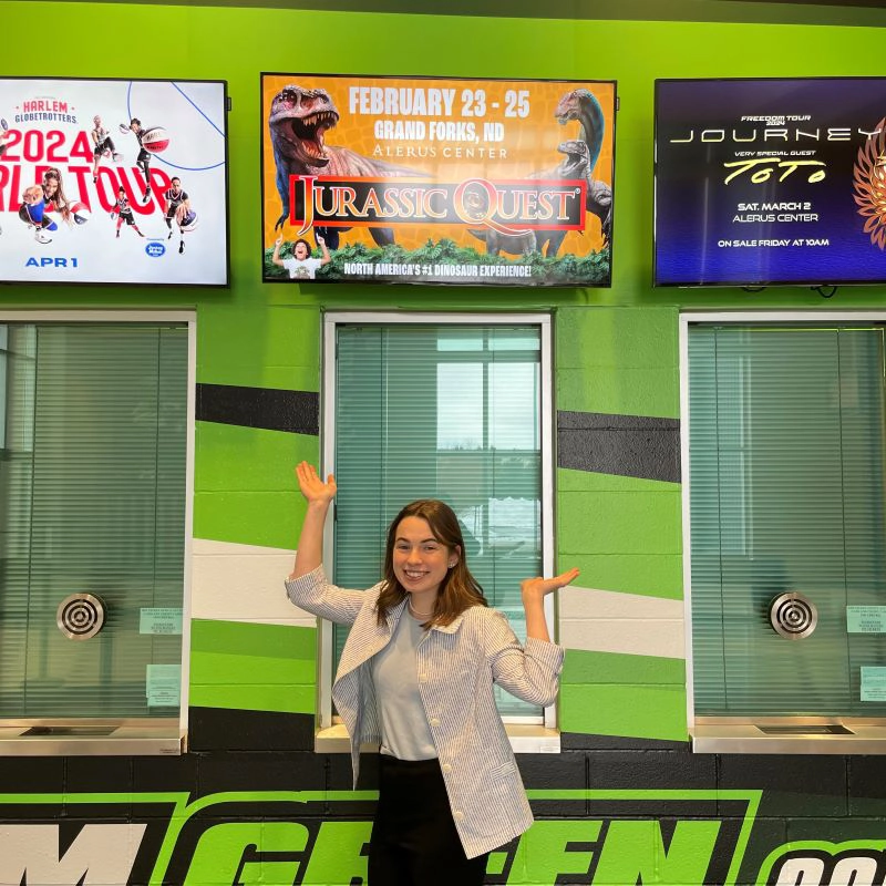 Woman stands in front of sign that reads 'jurassic quest' at the Alerus Center in Grand forks.