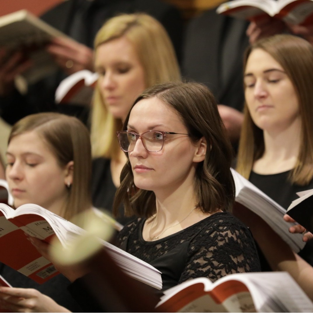 Four woman stand on choir risers, holding sheet music for Handel's Messiah