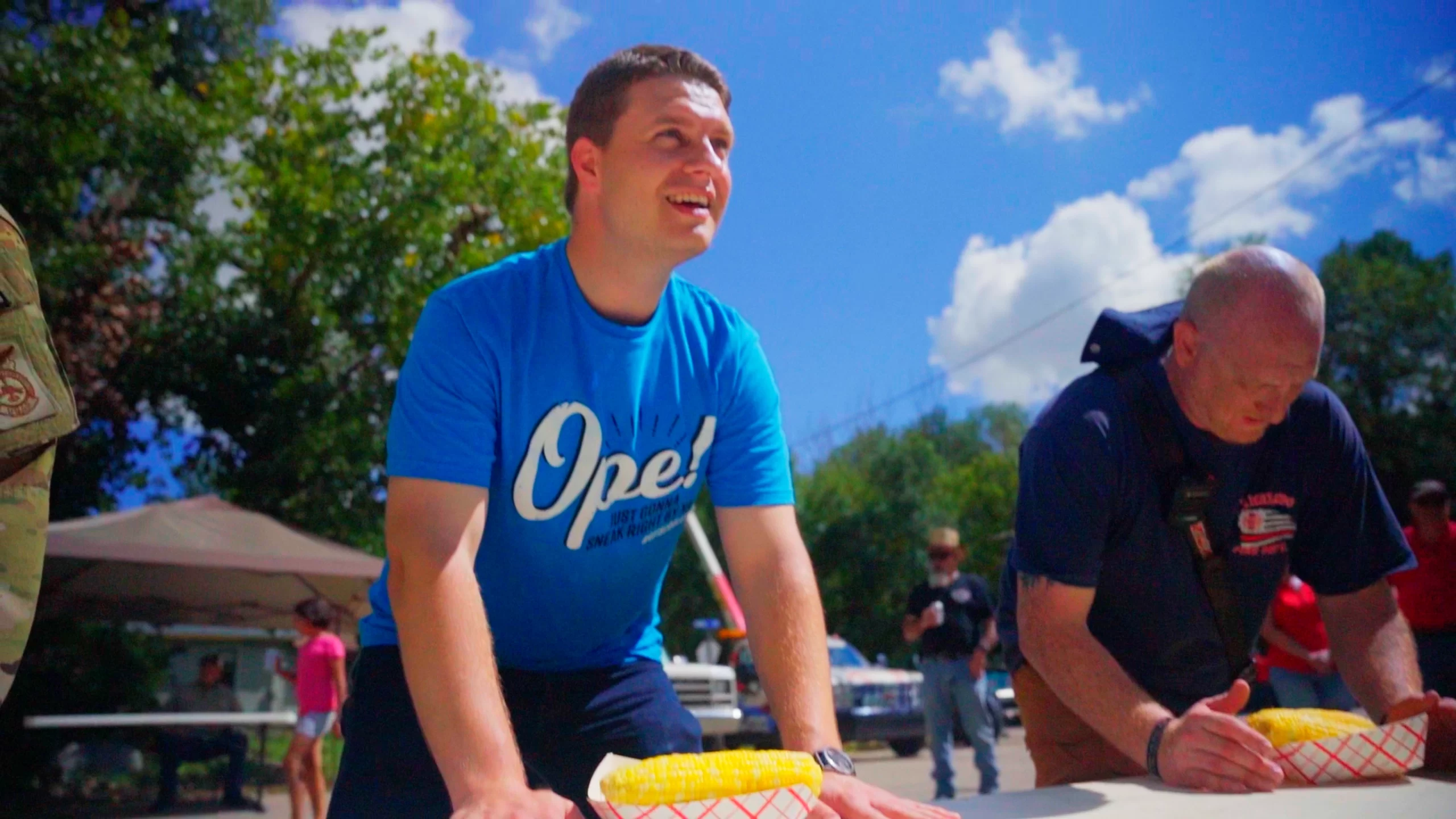 Grand Forks is Cooler article picture. Colin wears blue shirt that reads "Ope!" and participates in Emerado Corn Feed.