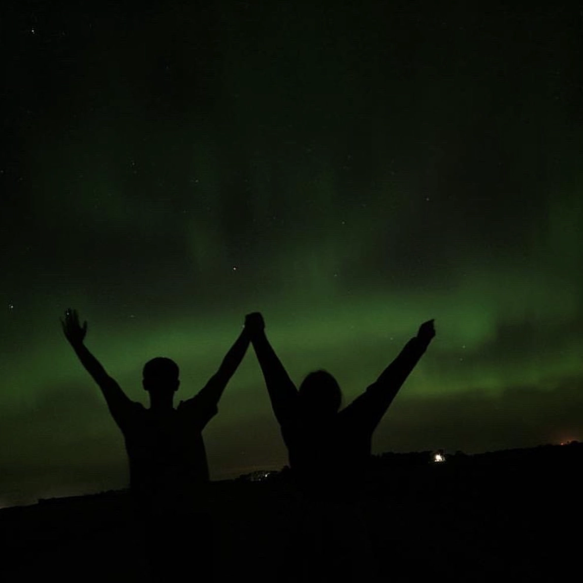 Two people holding hands watching the northern lights in Grand Forks.