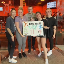 5 people stand with the Orange Theory 'brag board' that reads 'day 11' in Grand Forks.