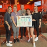 Five people, including writer Henessy, hold a "brag board" at Orange Theory Fitness