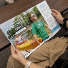 Two hands are pictured holding a spread within the Grand Forks Relocation Guide.