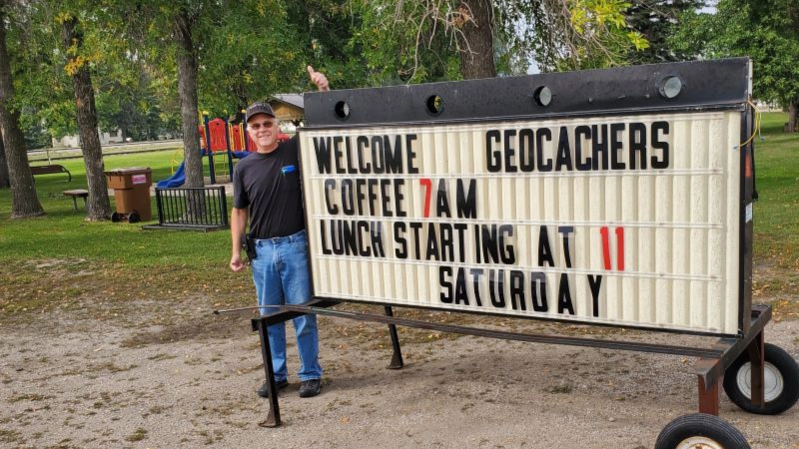 Geocaching in the Greater Grand Forks Region. Man stands in front of sign that reads "Welcome Geocachers."