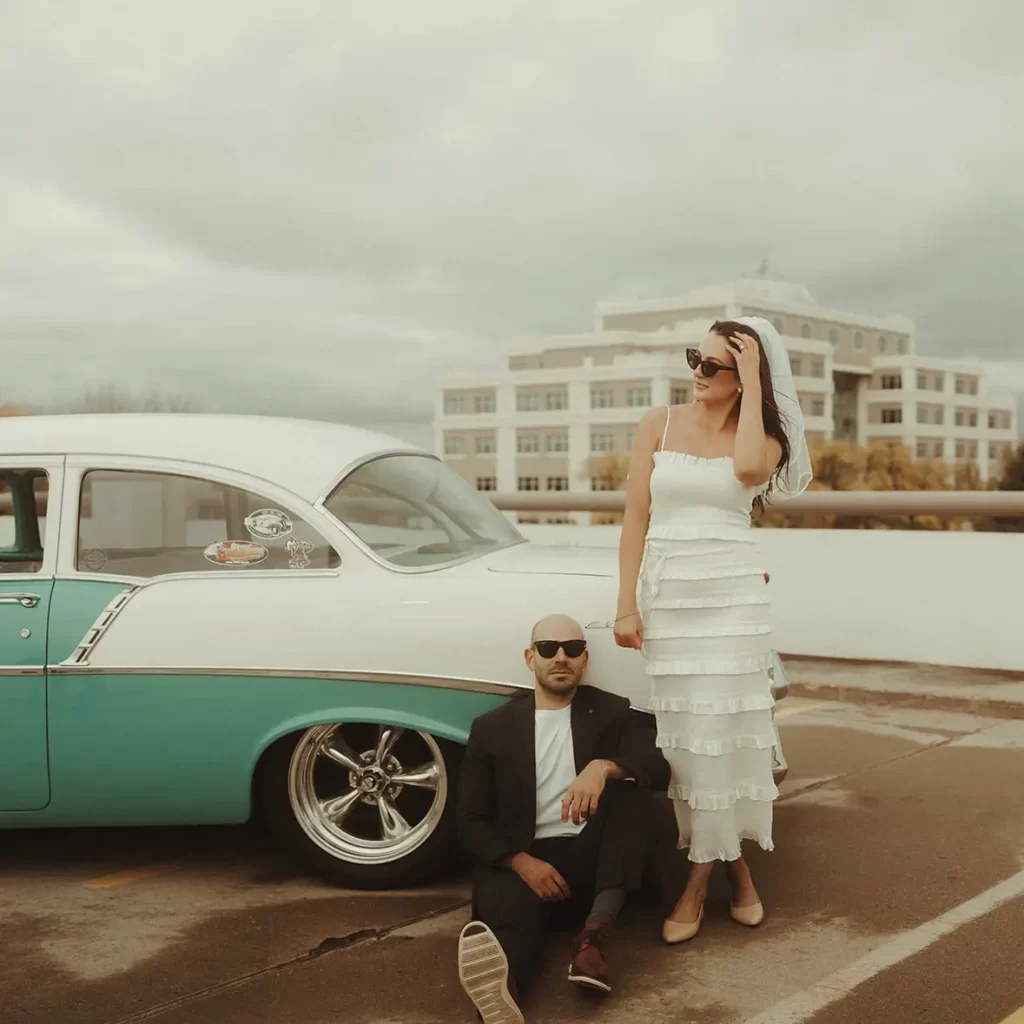 Couple stands next to vintage car on Grand Forks parking ramp for engagement photoshoot.