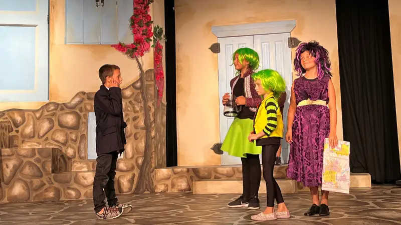 Grand Forks Community theater scene where 4 kids stand on stage in vibrantly colored costumes