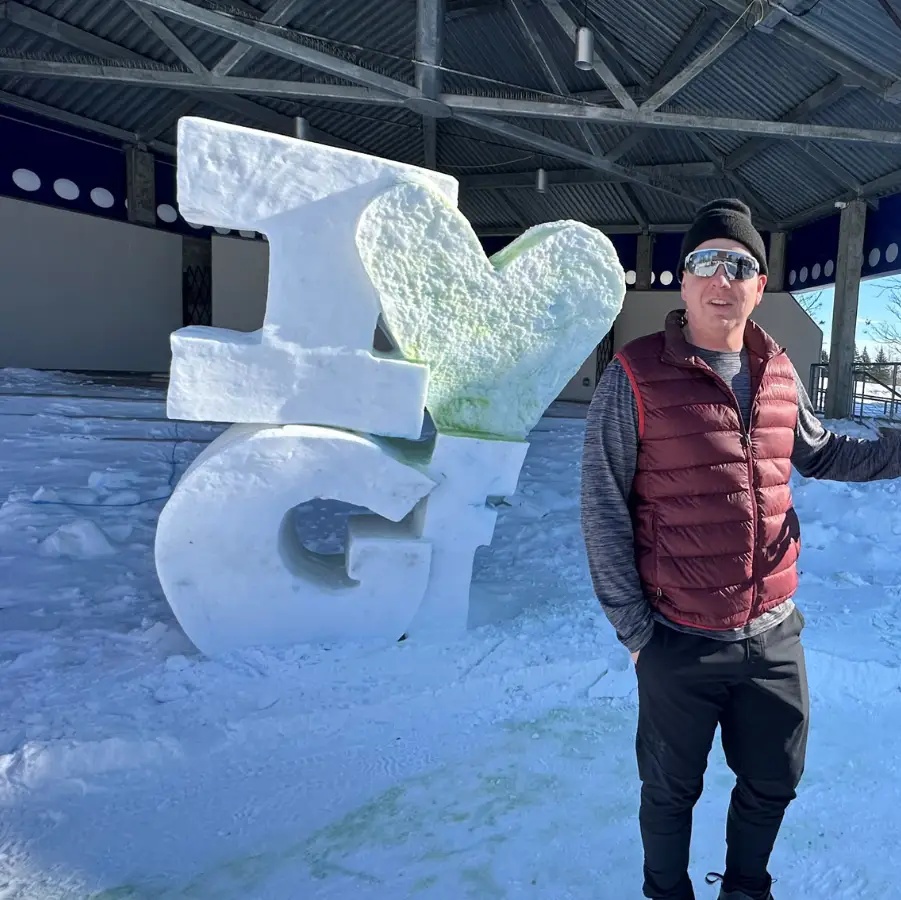 Grand Forks Author Paul stands with friend in Townsquare next to ice sculpture that reads 