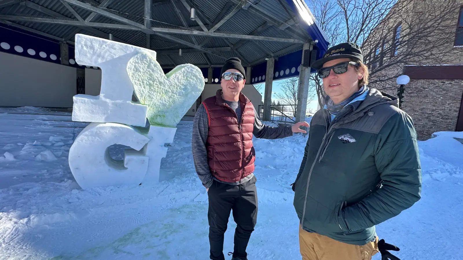 Grand Forks Author Paul stands with friend in Townsquare next to ice sculpture that reads "I Love Grand Forks"