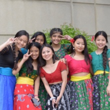 A group of seven young women smile at the camera dressed in colorful, traditional Nepalese garments.