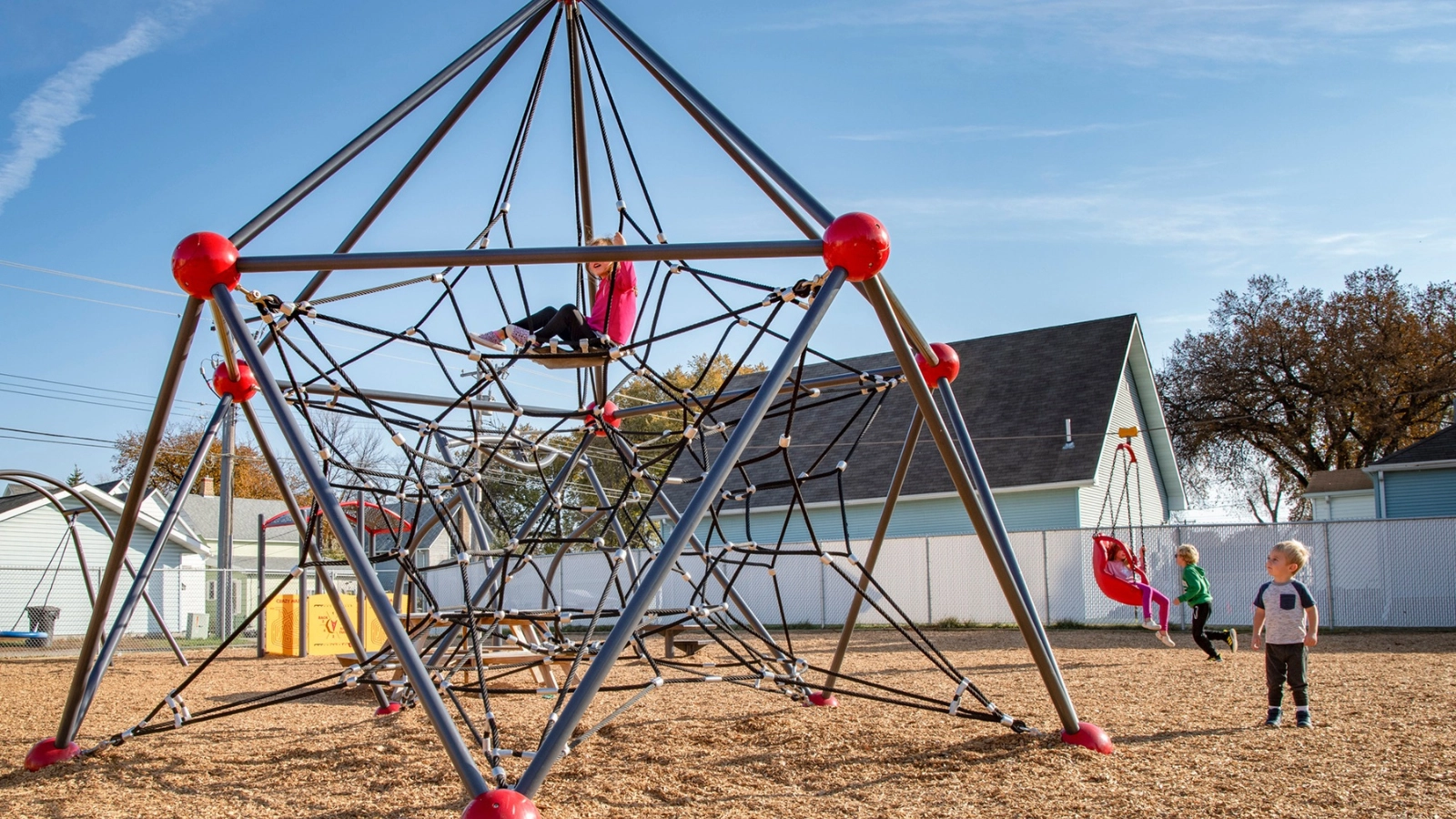 Three kids play on a spider web structure at a Grand Forks park.