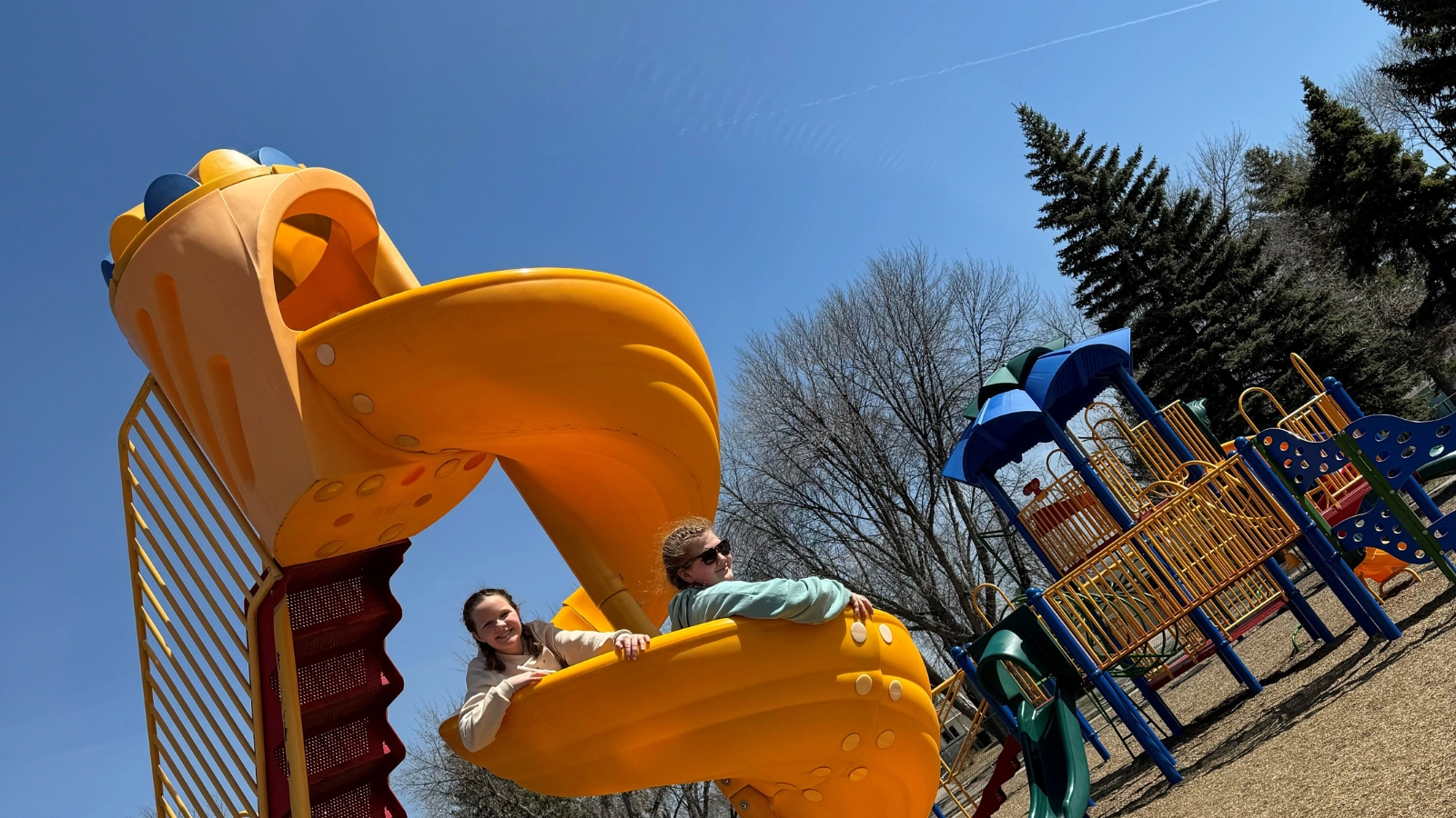 Two girls peak their heads over a yellow slide at a Grand Forks park.