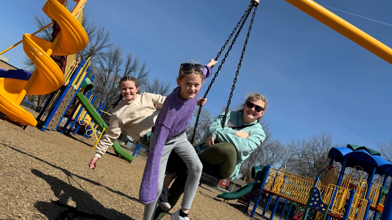 Three girls play on a tire swing at the park with slide in view.