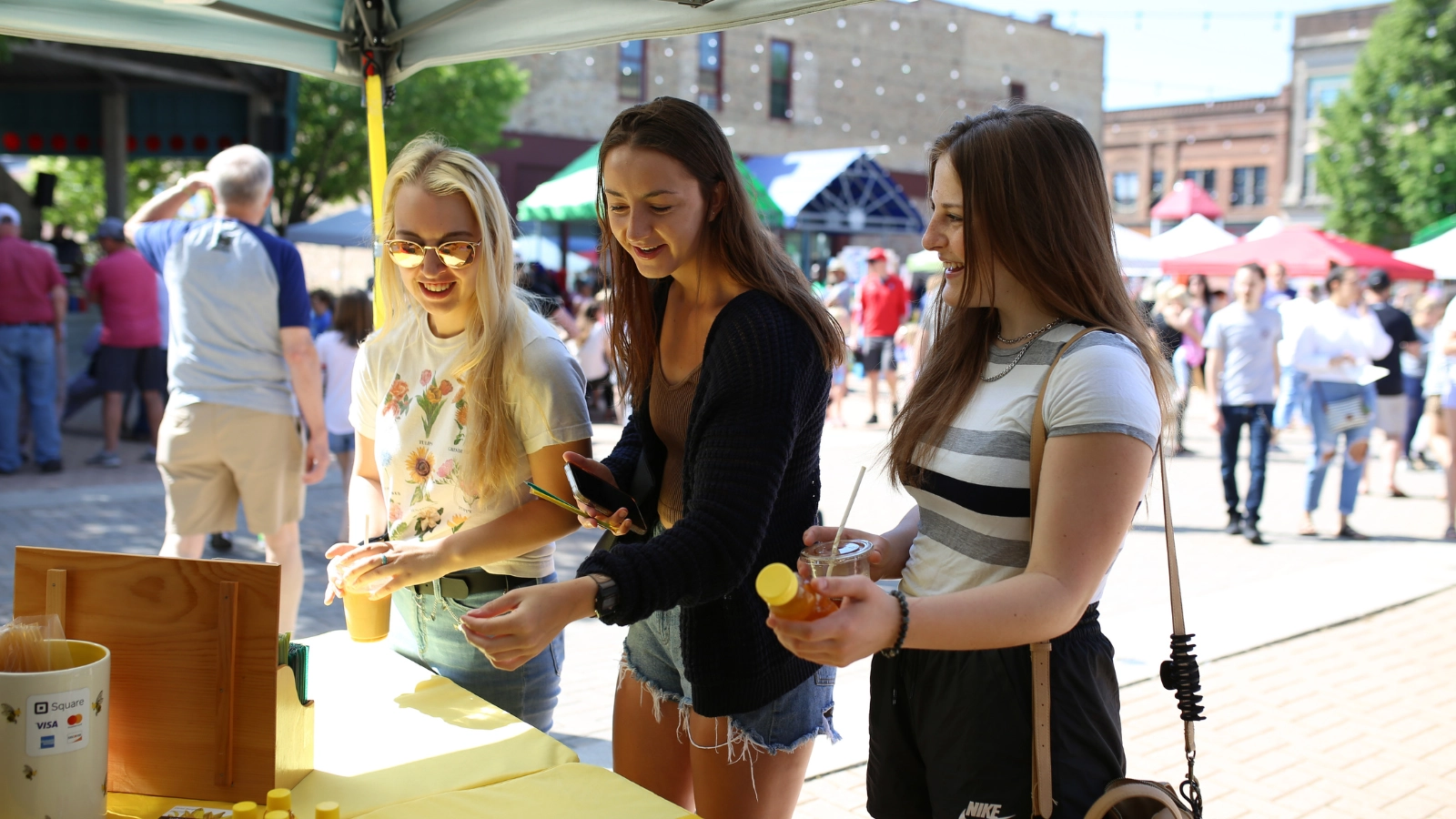 Three girls buying honey at Town Square Farmer's Market in Grand Forks.