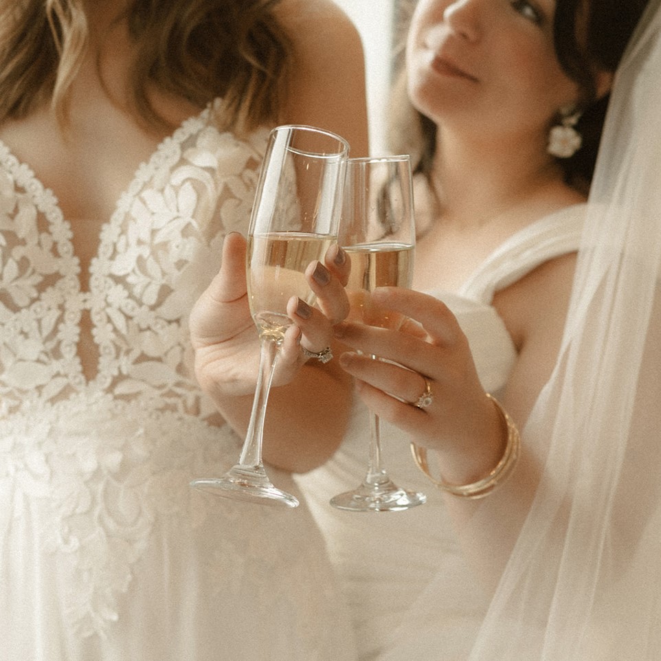 Two brides clink their champagne glass together on their wedding day.