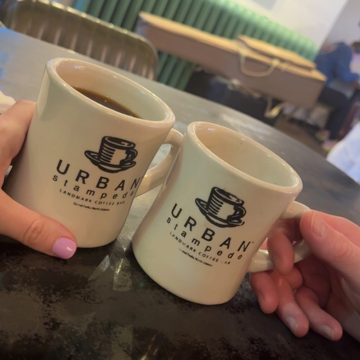 Two mugs clinking that read 'Urban Stampede' in Grand Forks.