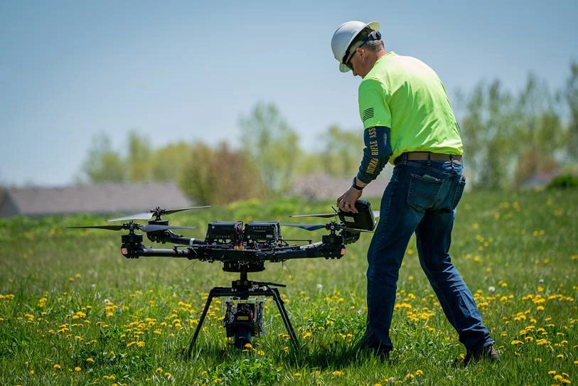 UAS small drone in a field with a man in a bright green shirt in Grand Forks.