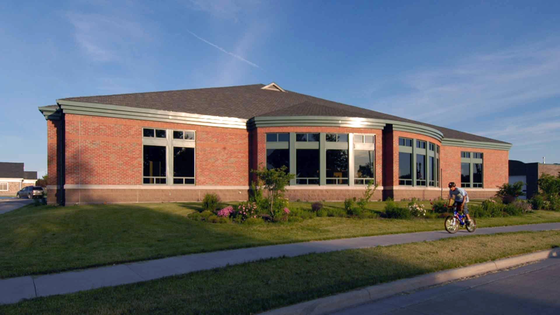 A red brick building with a large dome bay window sits among a well-trimmed grass lawn.