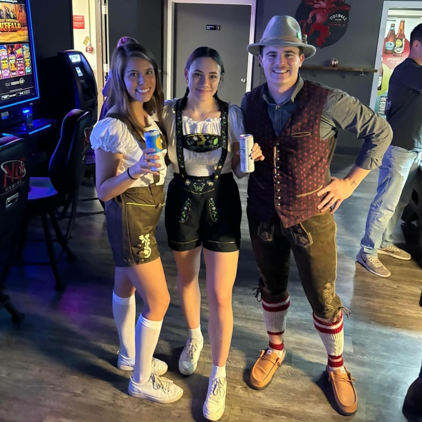 Three patrons dressed in Oktoberfest related costumes smile and hold their drinks in the Loft in downtown Grand Forks