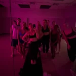 WCT author Isabelle takes a mirror selfie with nine other members of her workout class. The room is lit red and everyone is dressed in workout attire.