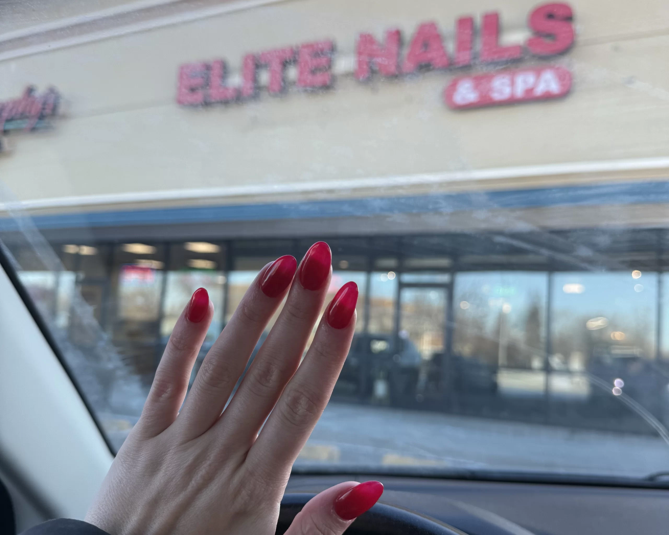 WCT author Isabelle flaunts her new red manicure in front of a nail salon storefront that reads "Elite Nails & Spa"