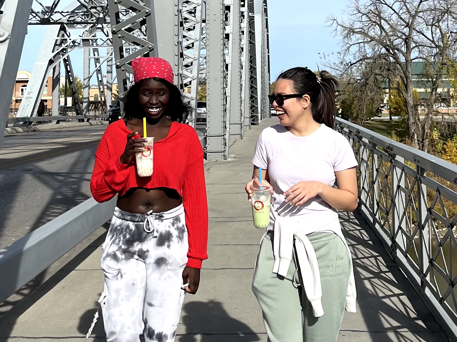 Two girls walking across the bridge in Grand Forks with teas from Tea & Crepe