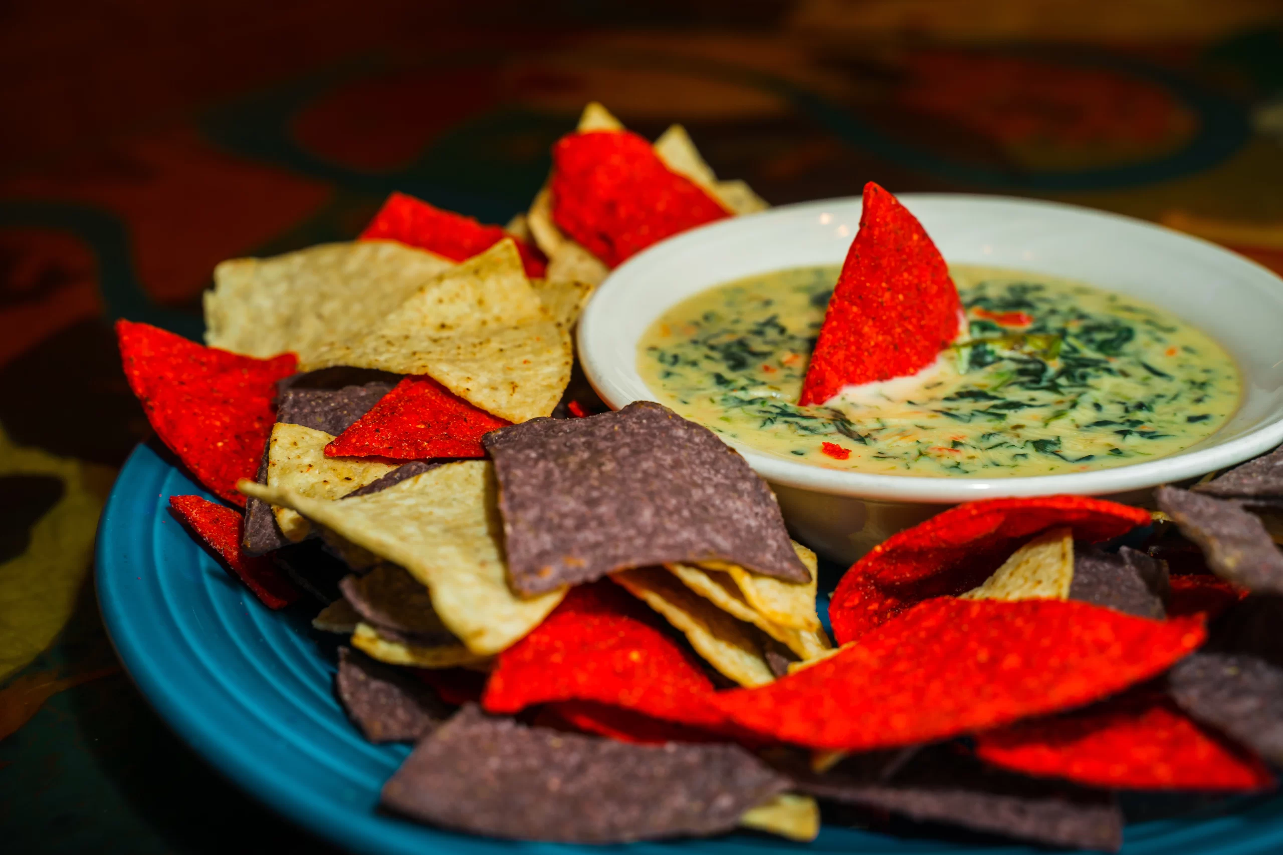 Red, black, and white tortilla chips surround a bowl of creamy spinach queso.