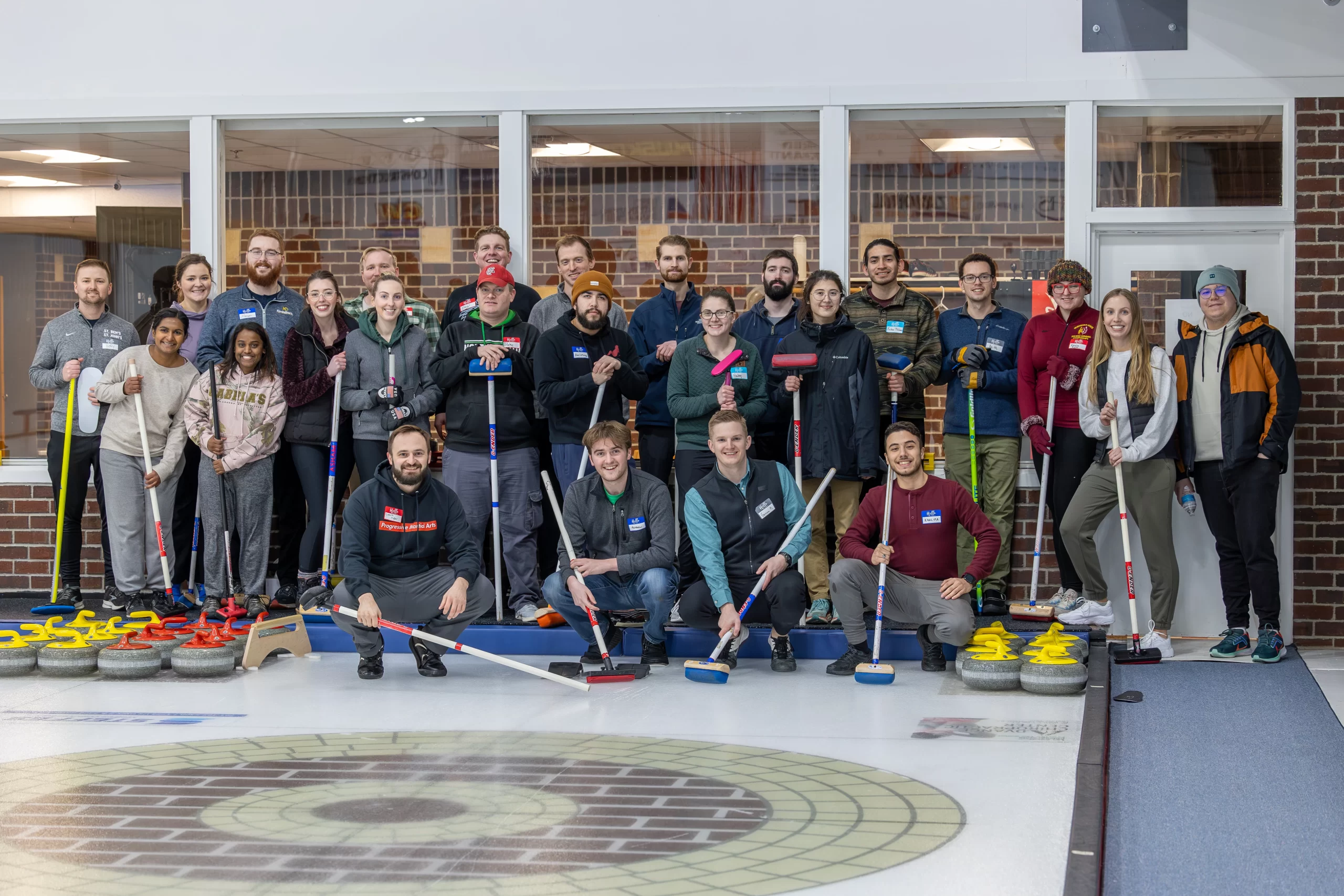 Grand Forks winter activities. A curling group stands together with curling equipment at the Grand Forks Curling Club.