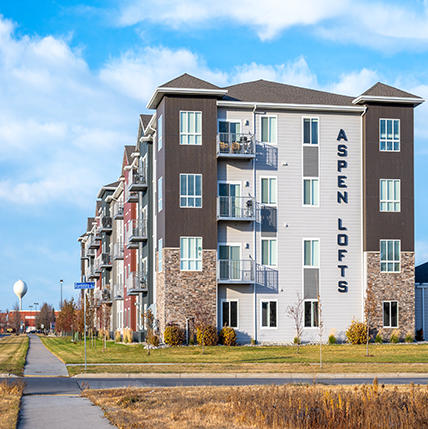 Aspen Lofts Apartments. A big complex with shades of beige and brown siding. Lots of windows and balconies showing.