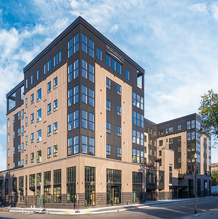 Exterior image of Franklin on 4th Apartments. Big tall building with tan and black colored accents. Loads of tall windows on the corners of the building and smaller windows for the individual apartments.