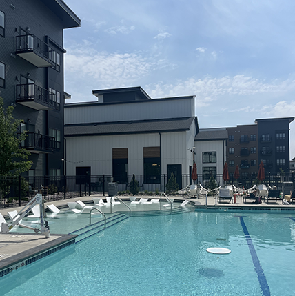 The District Apartments pool photo. A big pool with loads of chairs and space for swimming. The side of the building is black with balconies showing.