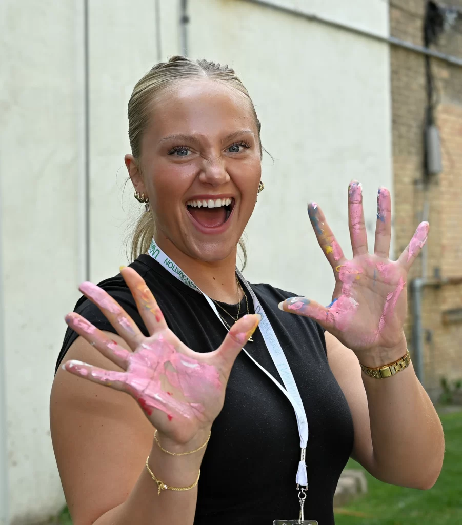 Author Isabelle poses in front of the camera with a big smile on her face. She is holding up both hands that are covered in pink paint.