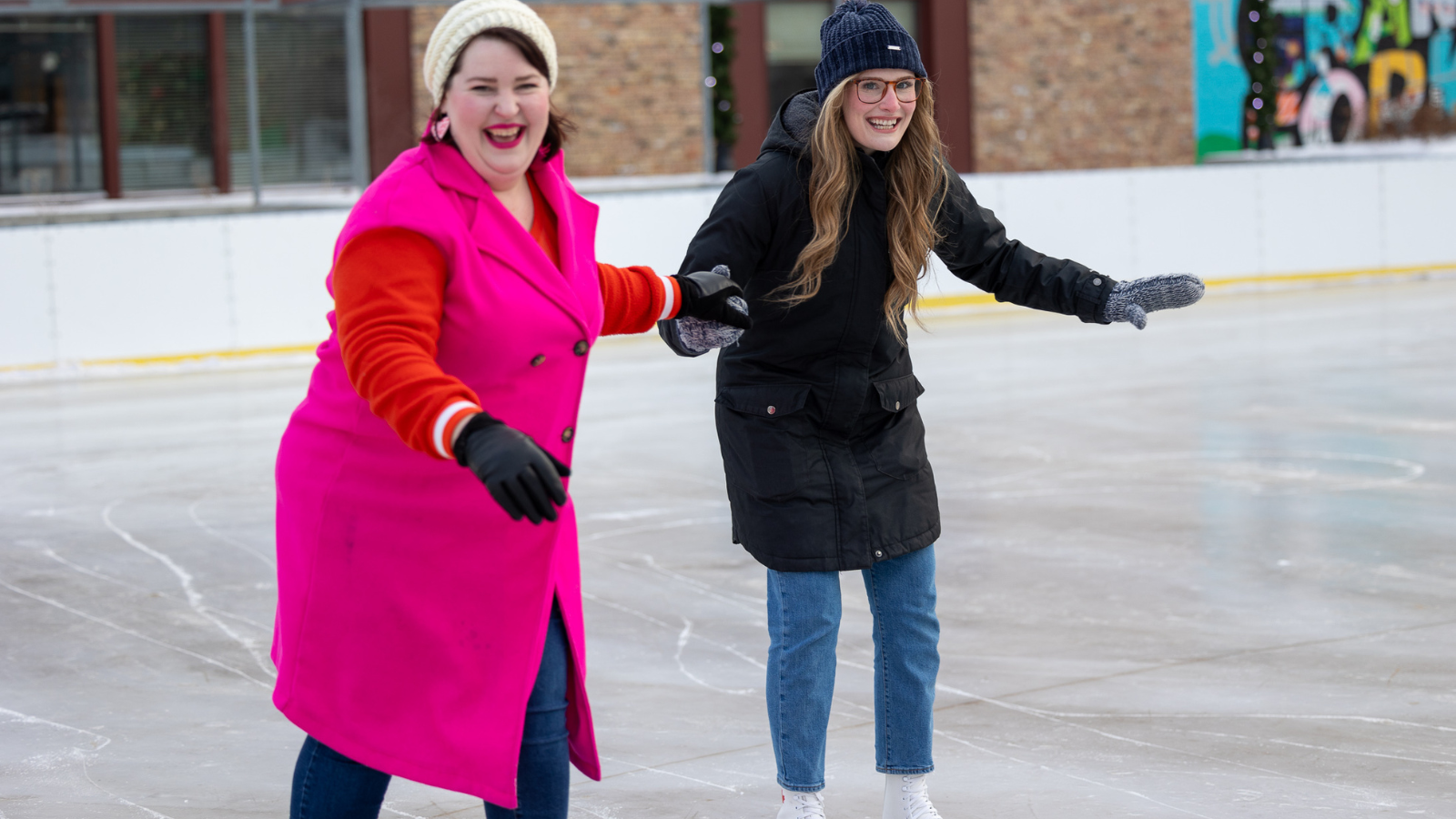 Becca and Friend skating at the downtown outdoor rink! they are holding hands and laughing.