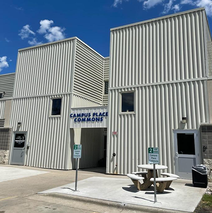 Exterior of Campus Place Apartments. Metal siding with a blue building sign and a picnic table out front.